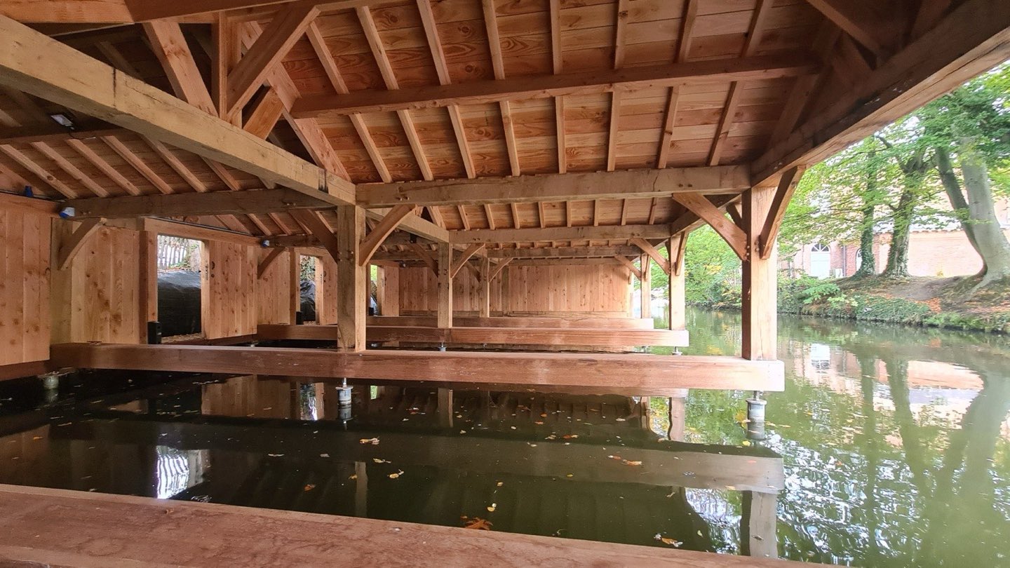 Binnenzicht van het botenhuis: houten spanten boven het water
