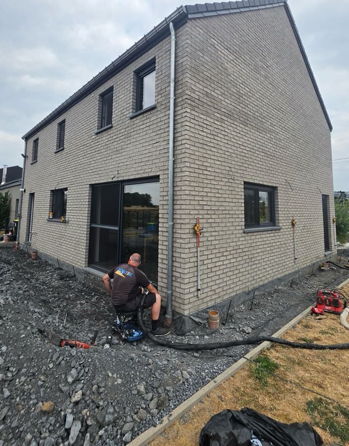 Technicien Soiltek injectant de la résine expansive le long de la façade d'une maison, avec récepteurs laser au mur