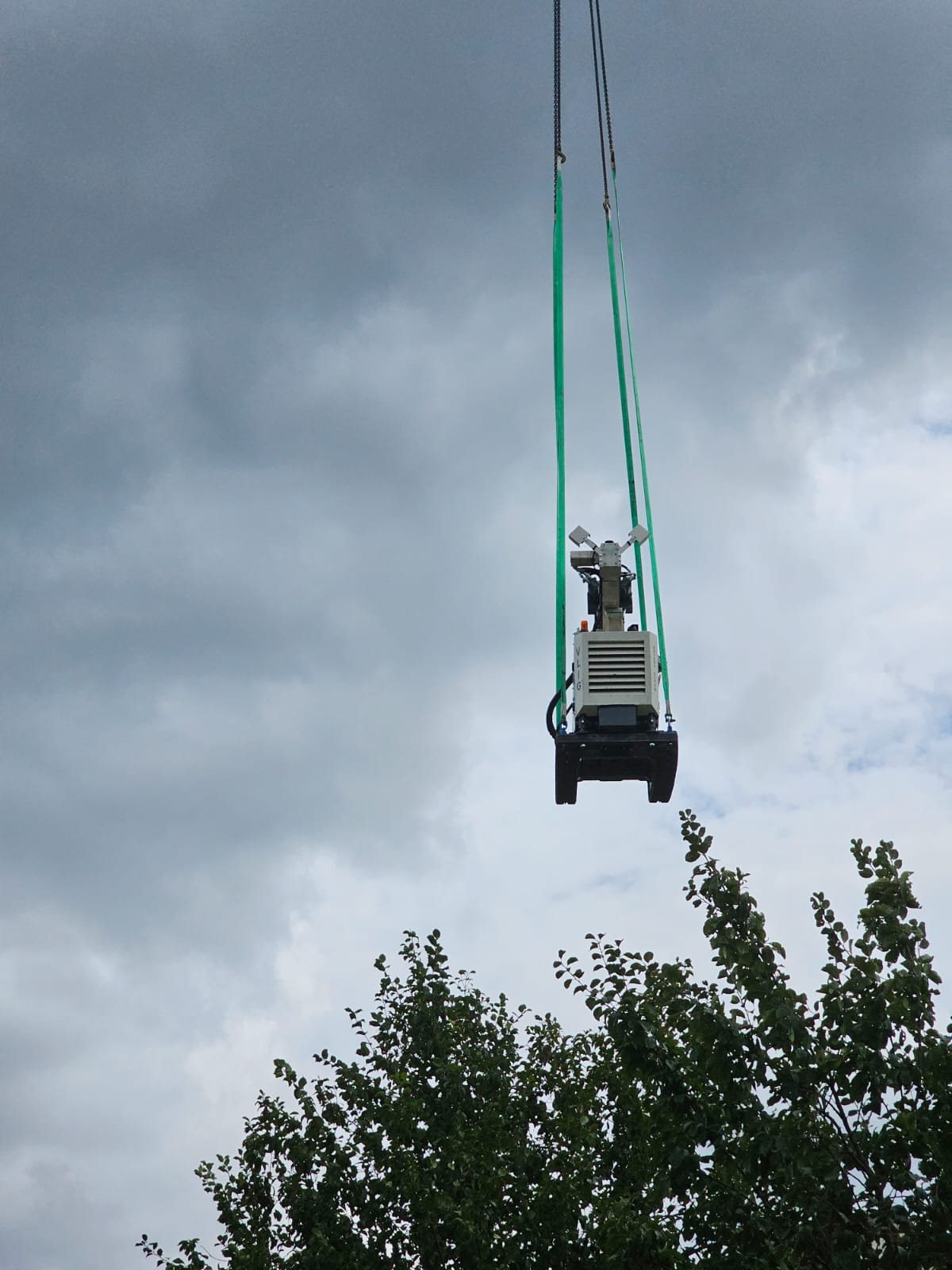 Compacte elektrische schroefmachine hangt aan hijsbanden onder een mobiele kraan