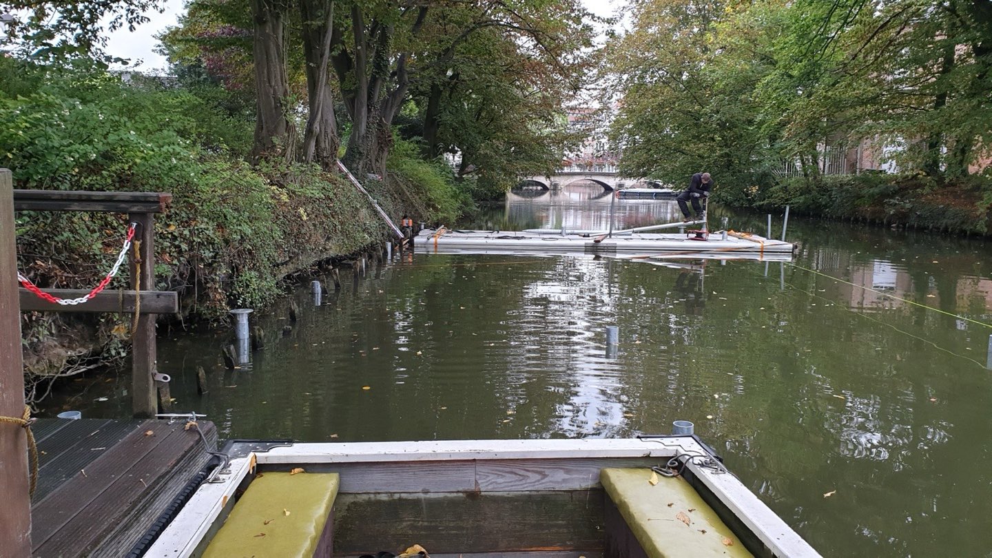 Werken vanaf een ponton op de rivier in Lier, met geplaatste palen langs de oever