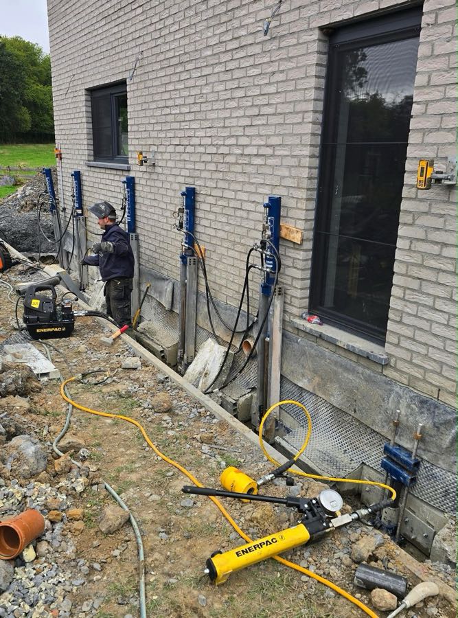 Rangée de vérins hydrauliques Magnum contre la façade d'une maison, avec un technicien et la pompe hydraulique