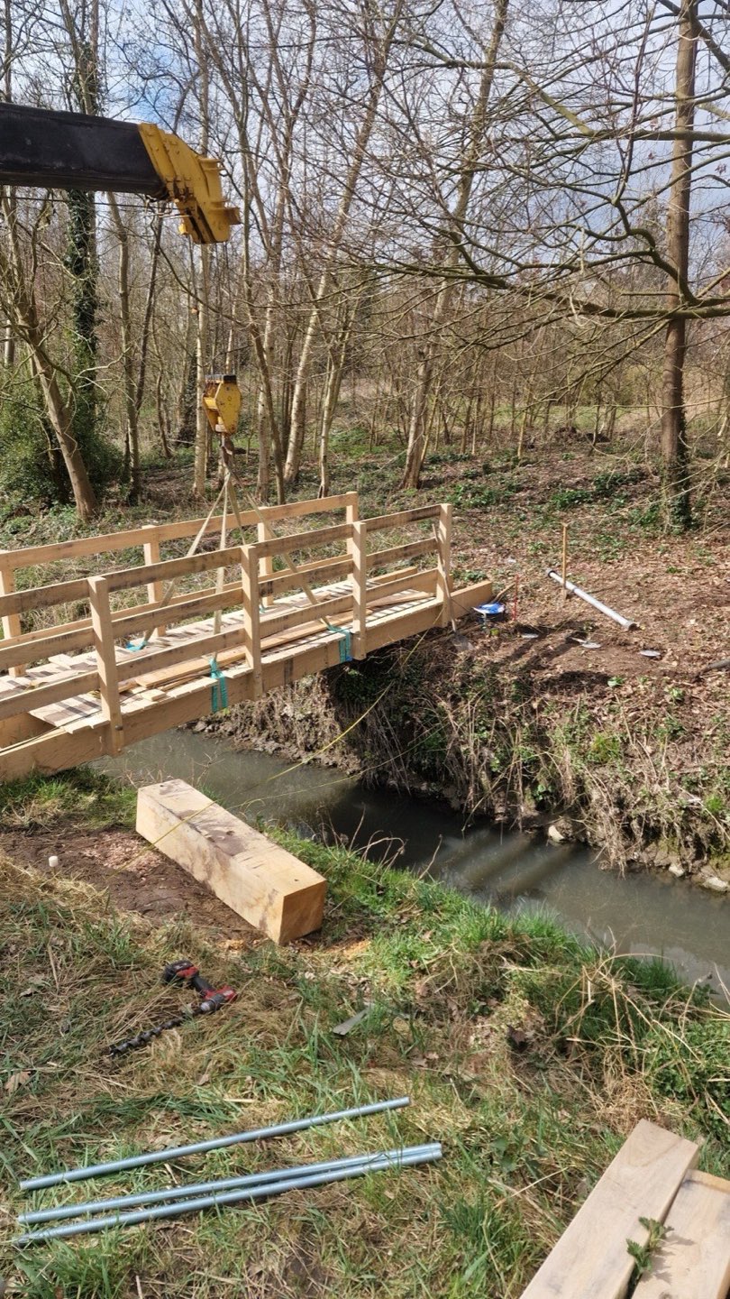 Houten voetbrug over een beek, gefundeerd op schroefpalen
